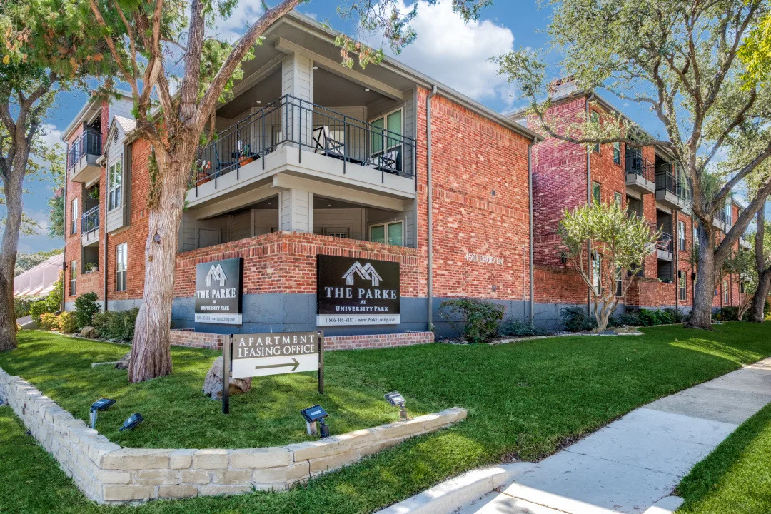 Three-story brick building with balconies beside the leasing office under blue skies