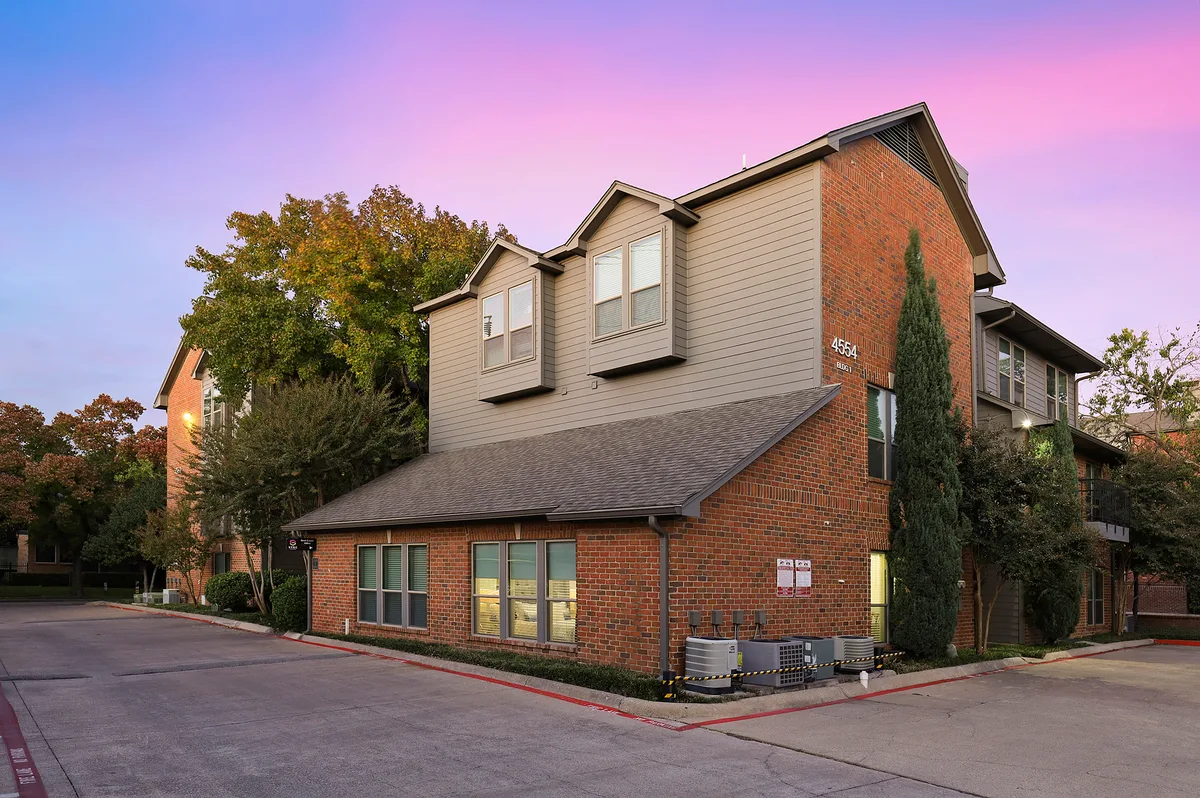 Brick and siding building with gabled dormers at dusk beneath a pink sky