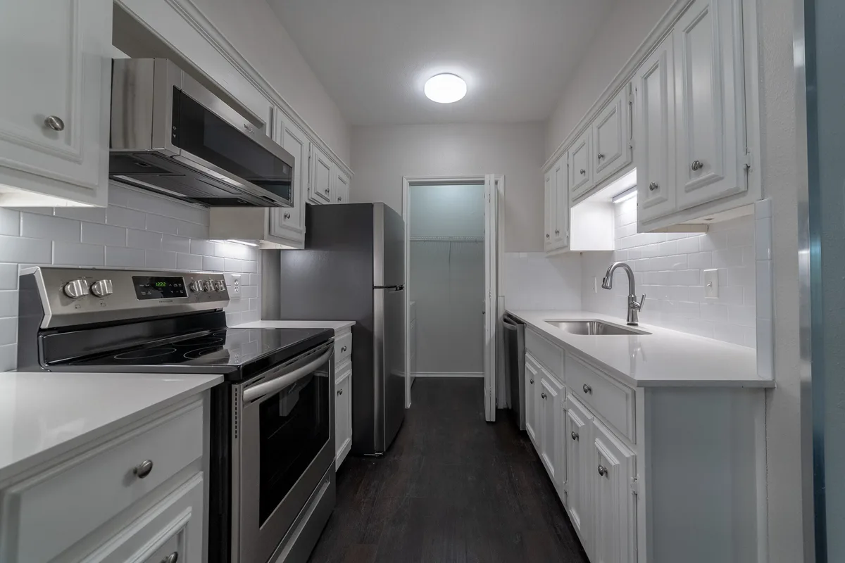 Galley kitchen with white cabinets, stainless appliances, and dark hardwood floors