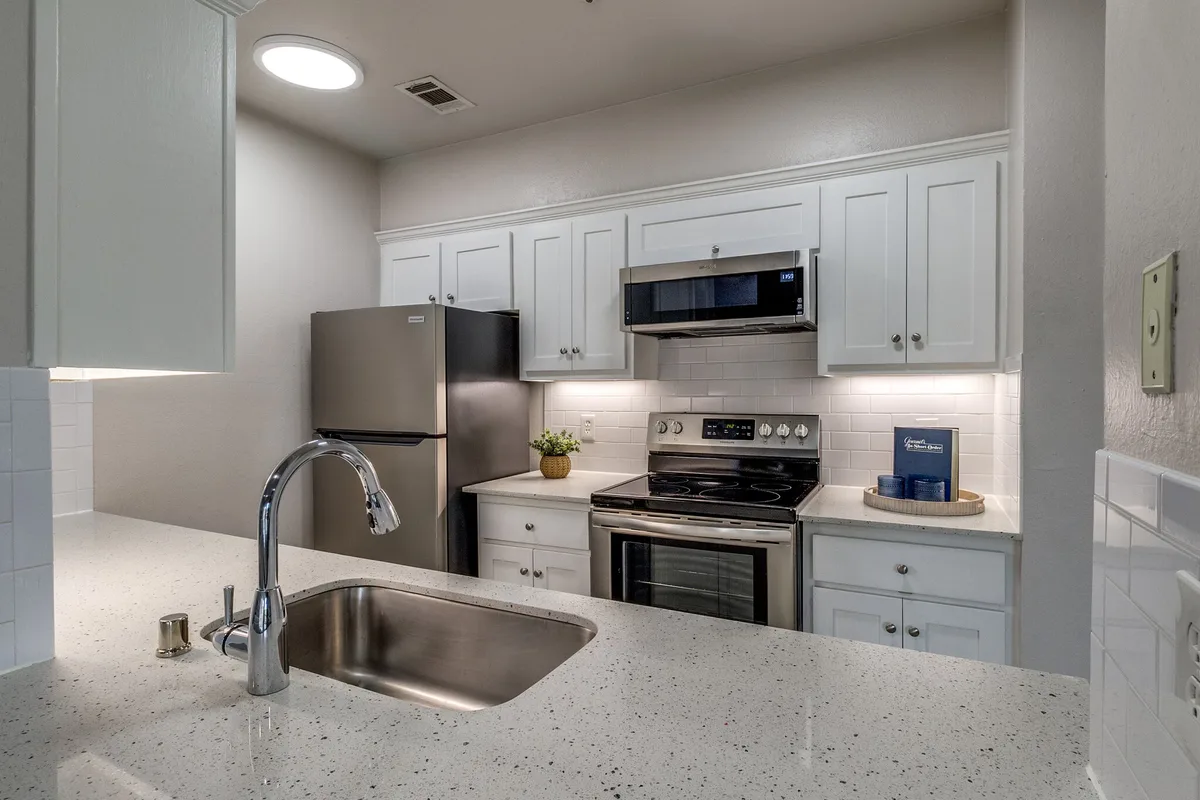 Kitchen with white cabinets, speckled quartz counters, and stainless appliances