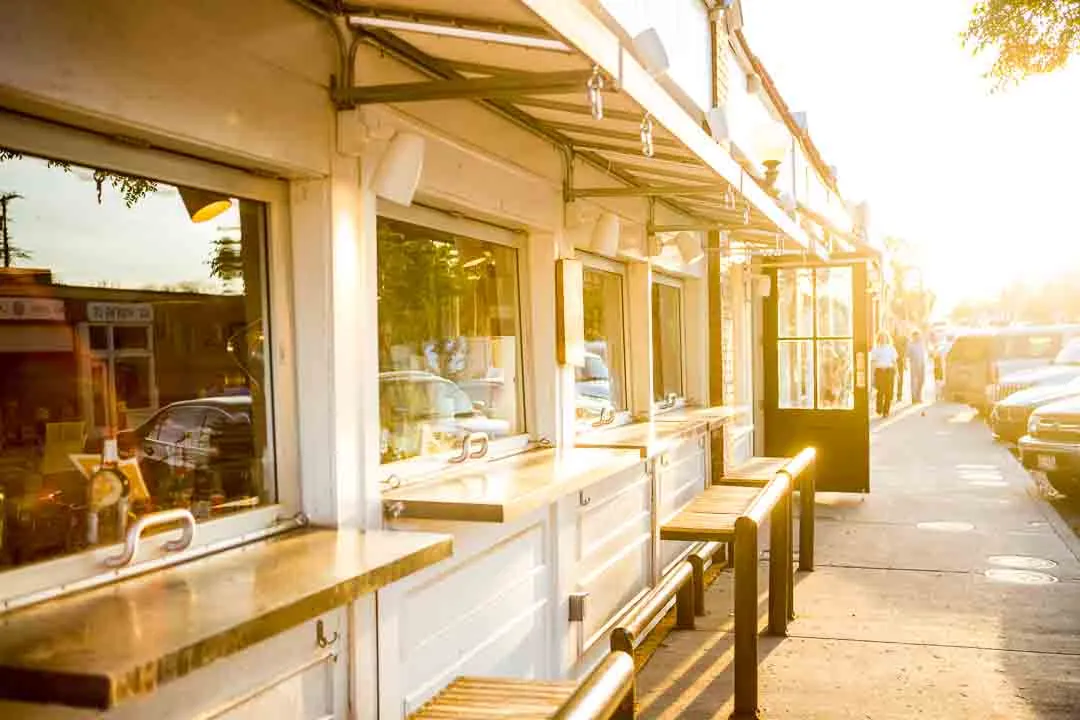 A sunlit cafe window bar with stools along a Bishop Arts sidewalk