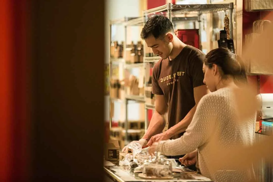 Two people making chocolate behind the counter of a Bishop Arts shop