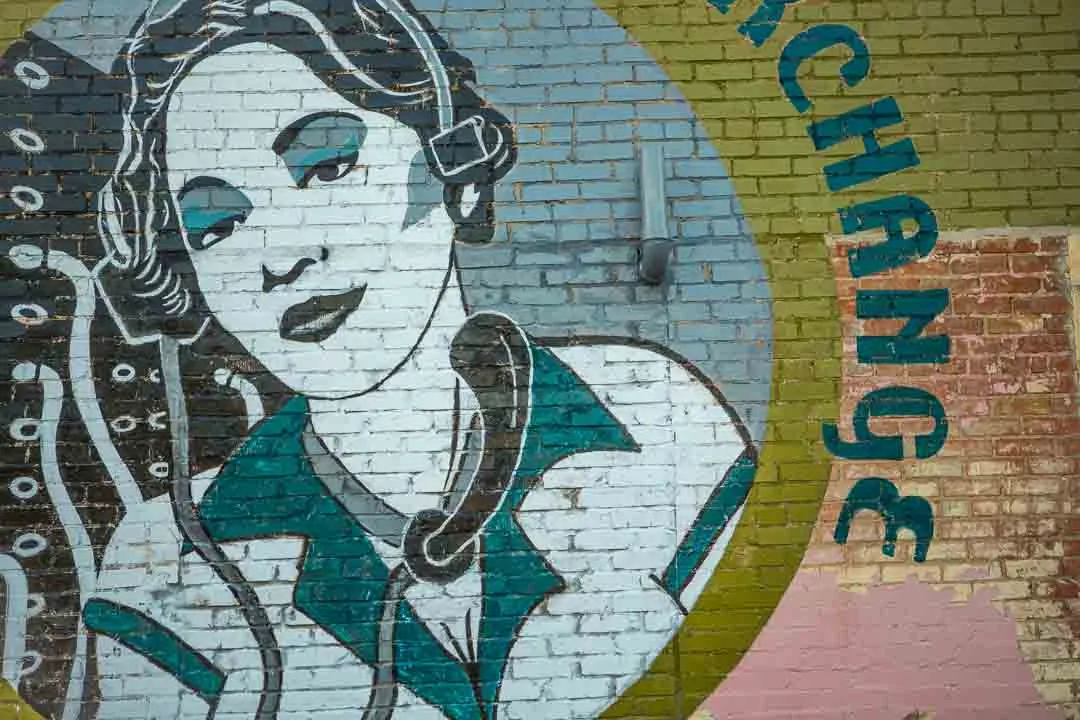 A painted mural of a woman wearing a headset on a brick wall