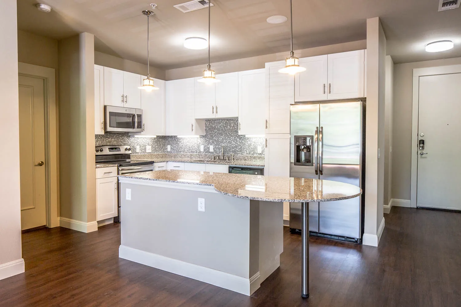 A kitchen with a granite island, stainless refrigerator and wood-style plank floors