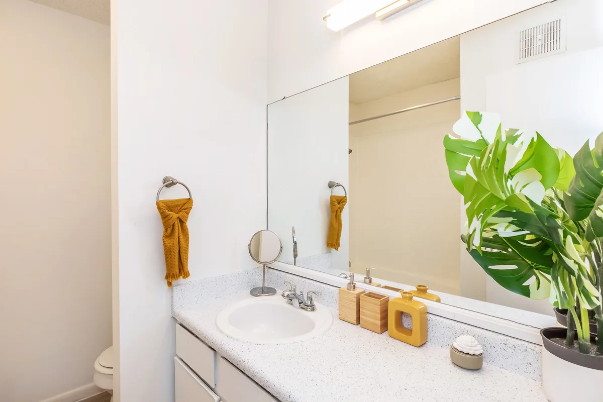 Bathroom vanity with speckled countertop, wide mirror, and overhead vanity lighting