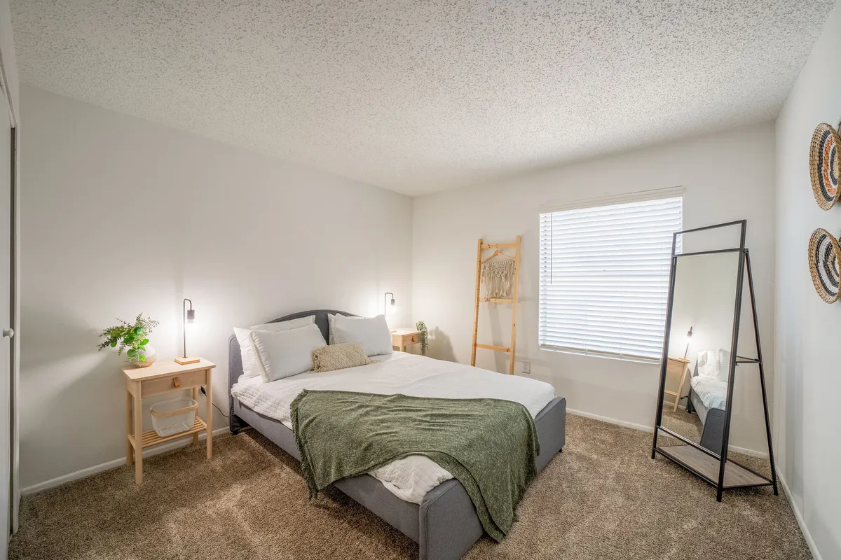 Staged bedroom with upholstered bed, wood nightstands, and a leaning floor mirror