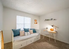 Second bedroom staged with a daybed and compact desk beneath a window
