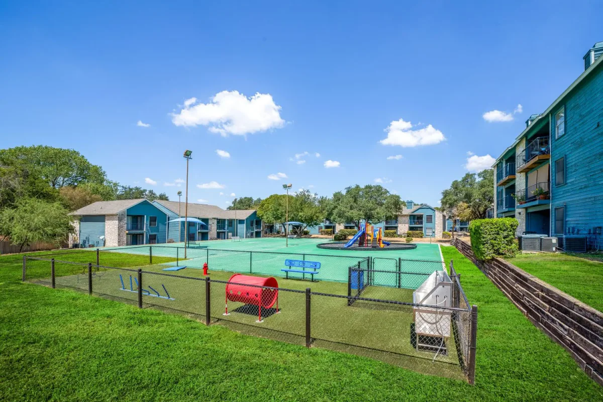Fenced dog park with agility equipment beside a sport court and playground