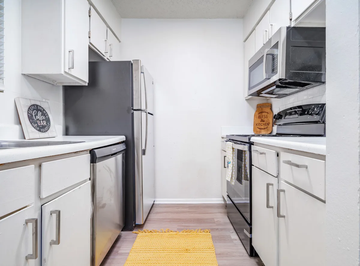 Galley kitchen with white cabinets, stainless refrigerator, and stainless range and microwave