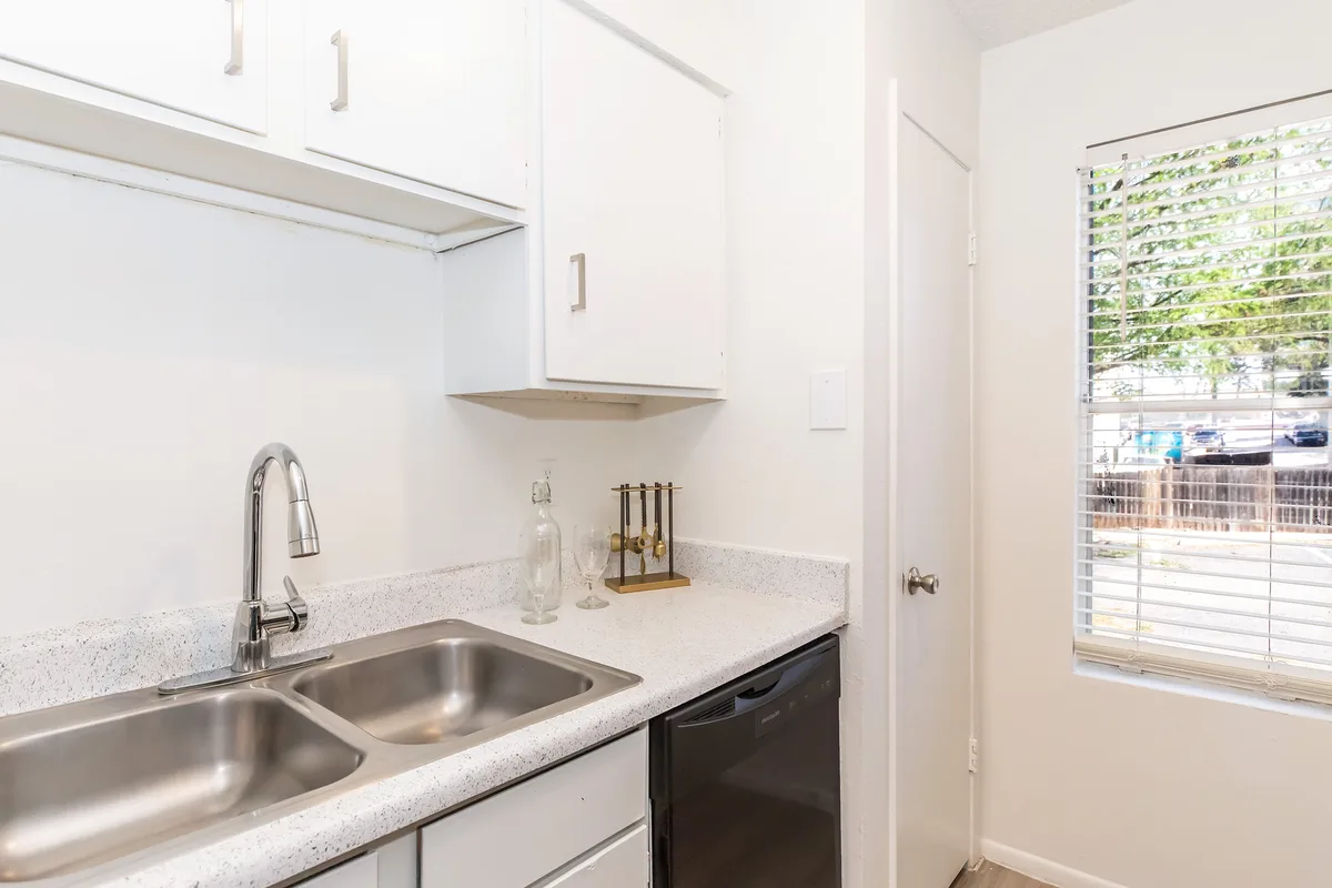 Kitchen with a double stainless sink, speckled white counters, and a bright window