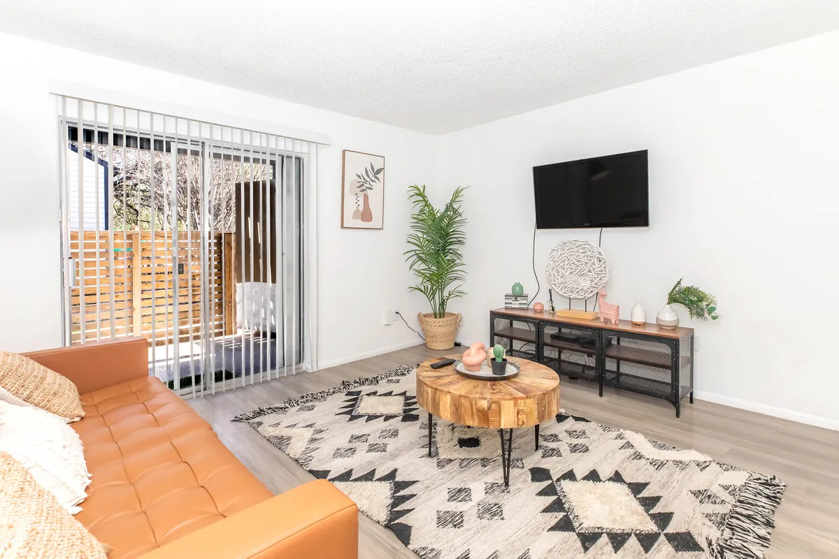 Living room with tan leather sofa, mounted TV, and sliding door to a private patio