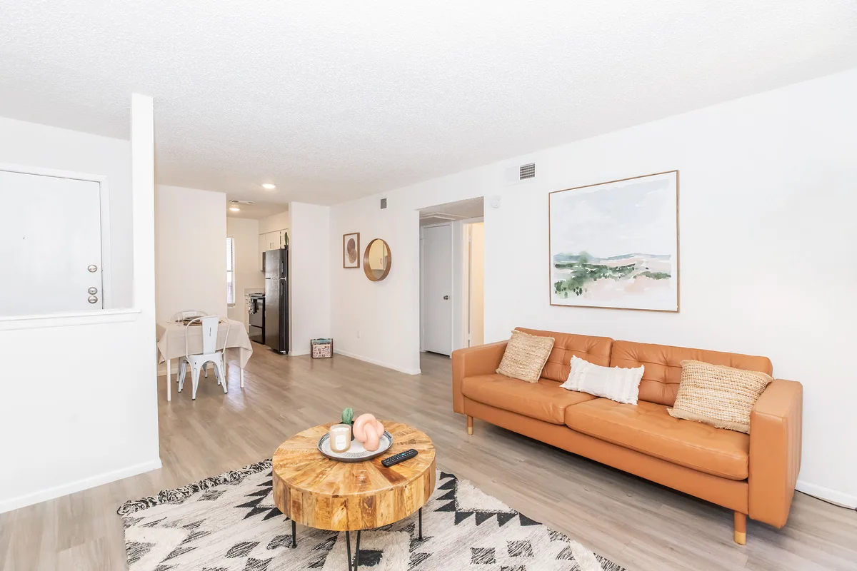 Open-concept living and dining area with tan leather sofa and wood-look flooring