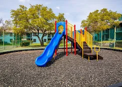Children's playground with a blue slide and climbing structure over mulched safety surfacing