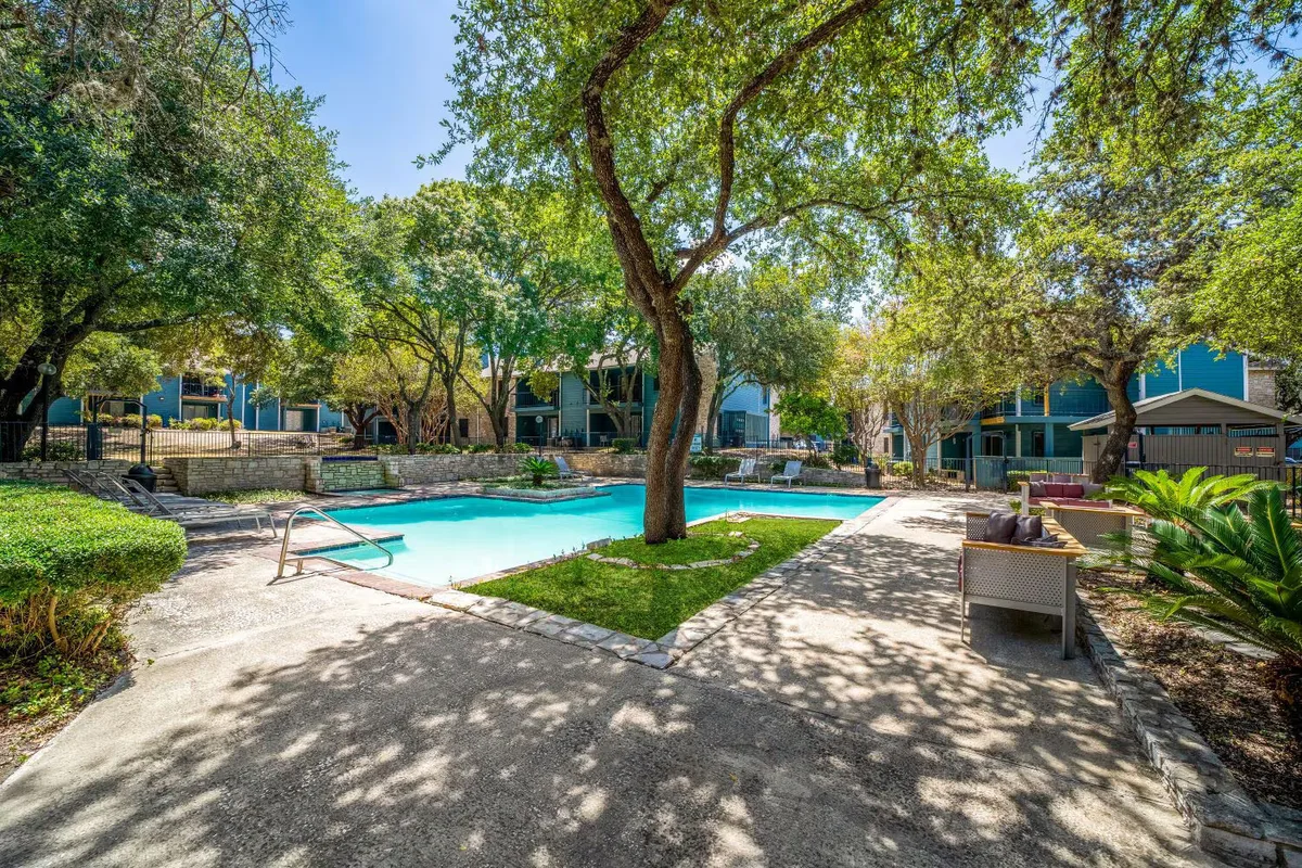 Resort-style swimming pool shaded by mature oak trees with poolside lounge seating