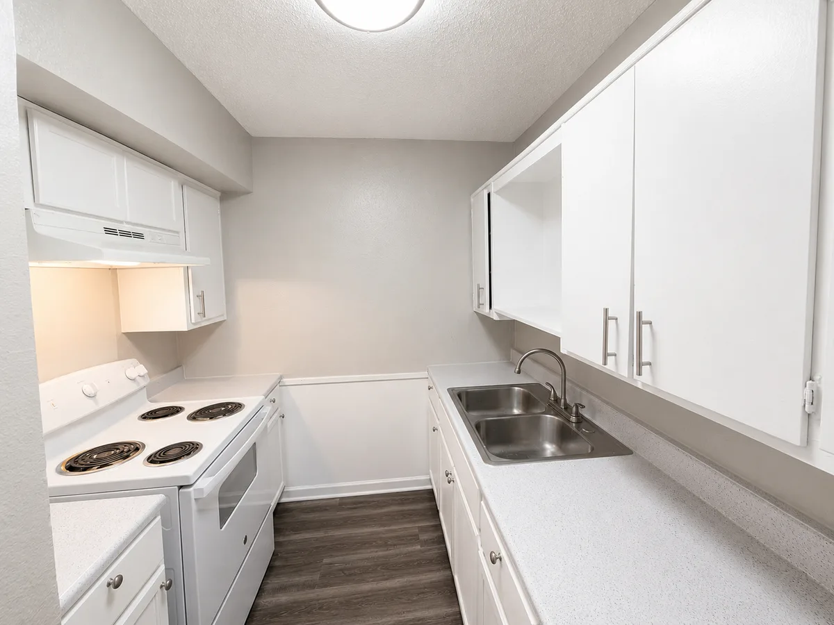 Galley kitchen with white electric range, double stainless sink, and ample white cabinets
