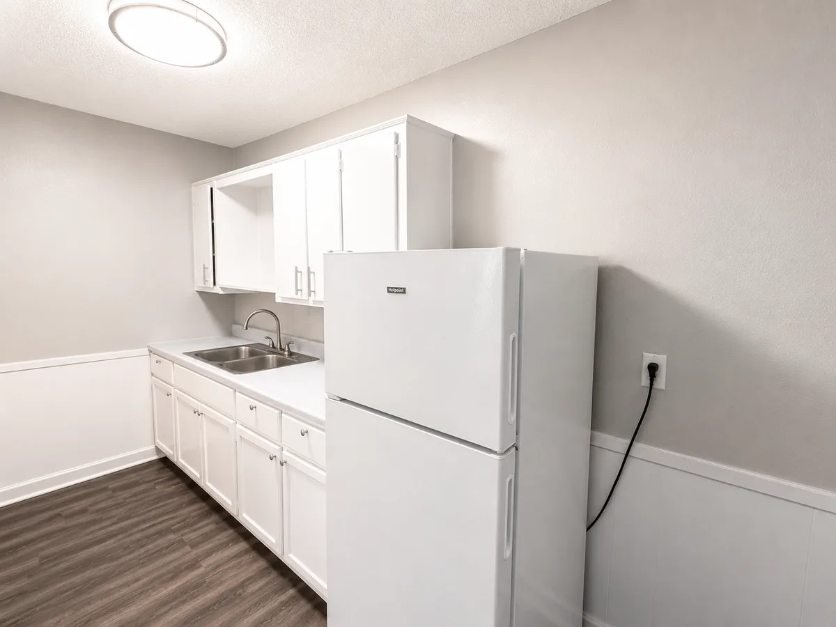Galley kitchen with white refrigerator, stainless sink, and bright white overhead cabinets