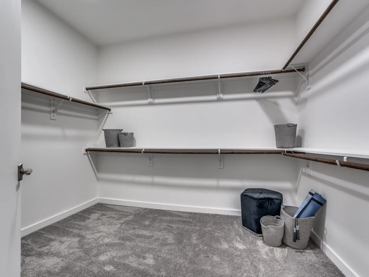 Spacious carpeted walk-in closet with wood shelving and hanging rods