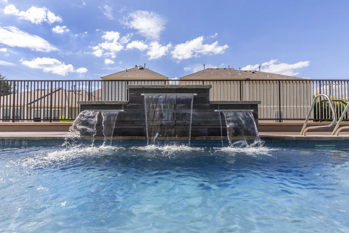 Resort-style pool with a three-chute stone water feature under blue sky