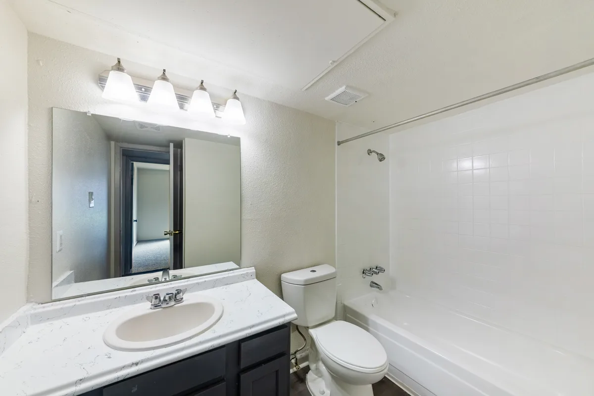 Bathroom with a tiled tub-shower surround, marble-look vanity, and large mirror