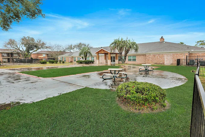 Open grassy courtyard with picnic tables and a gabled clubhouse under blue sky
