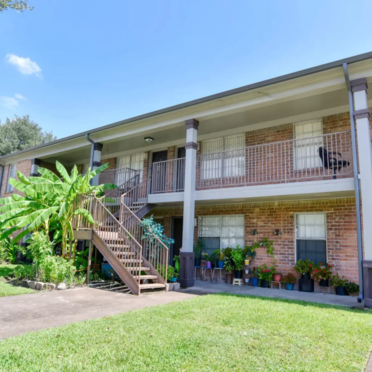 Two-story brick building with covered balconies, an exterior staircase, and resident patio plantings
