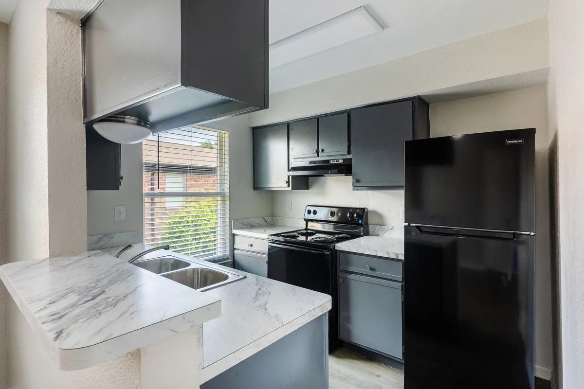 Kitchen with gray cabinetry, marble-look counters, black appliances, and a double sink