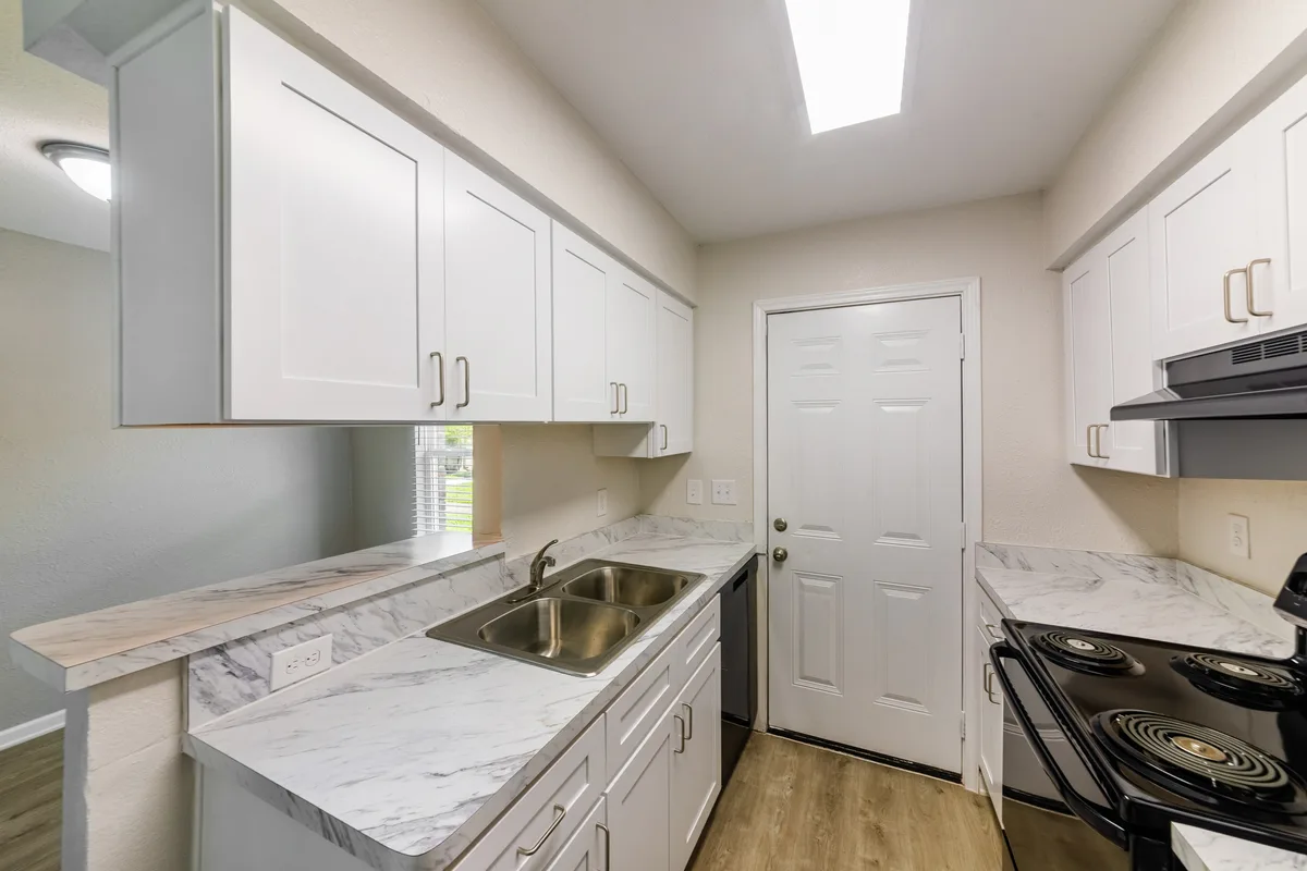 Galley kitchen with white cabinets, marble-look counters, and an exterior door