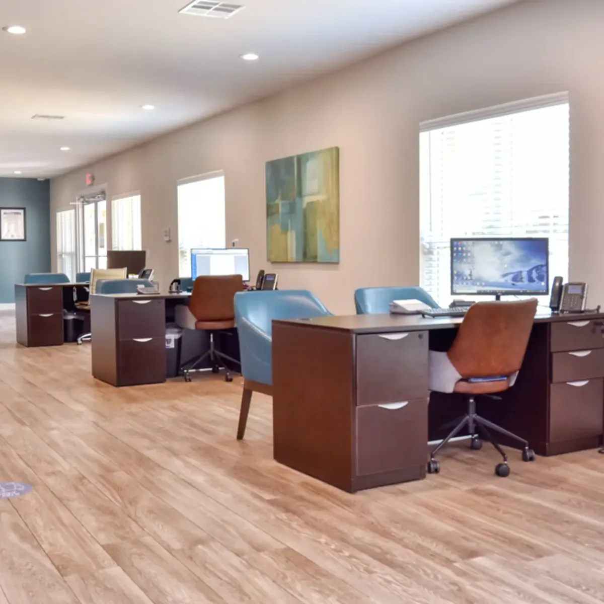 Leasing office with wood-toned desks, computer workstations, and blue accent chairs