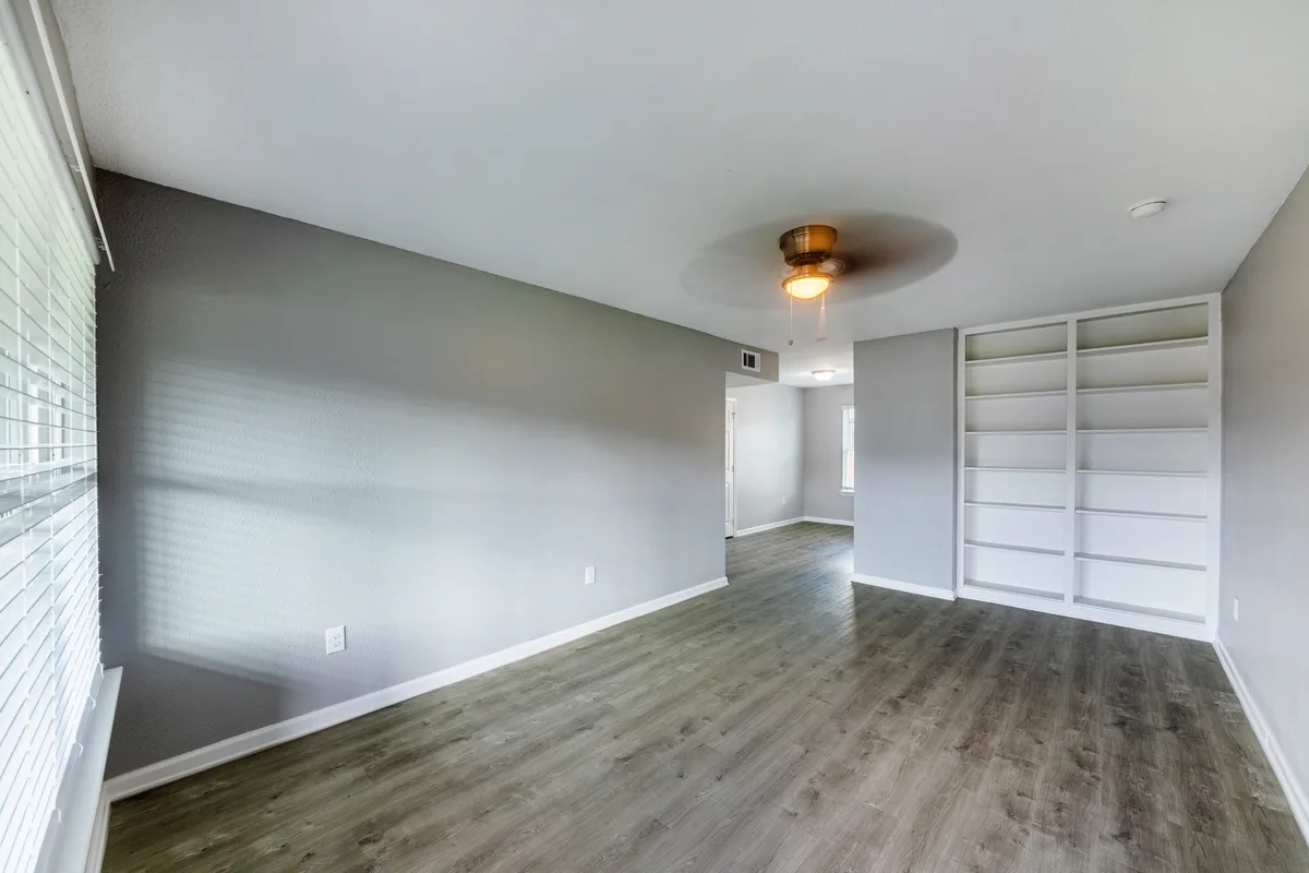 Empty living area with a gray accent wall, white built-in shelving, and ceiling fan