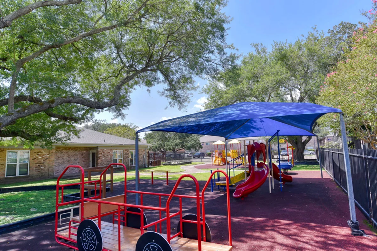 Shaded playground with a canopy-covered play structure, slides, and climbing equipment