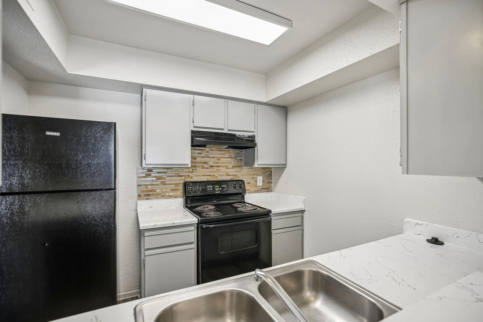 Two-bedroom kitchen with a stone backsplash, black appliances, and double sink
