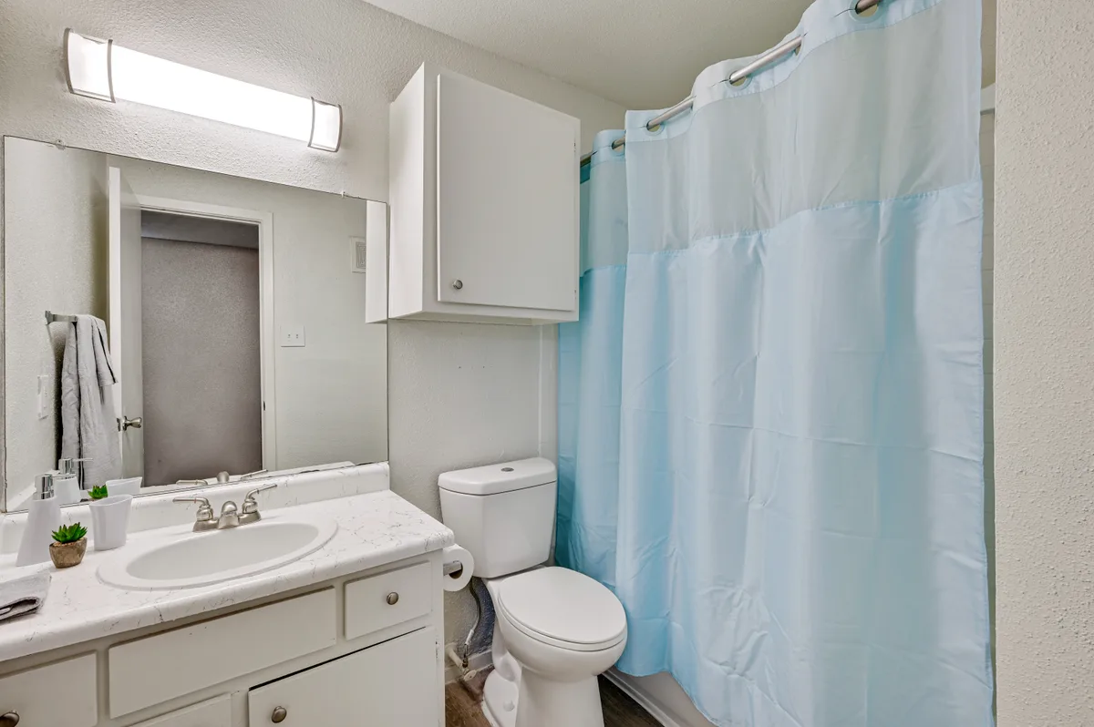 Bathroom with a white vanity, faux-marble counter, and tub with shower curtain