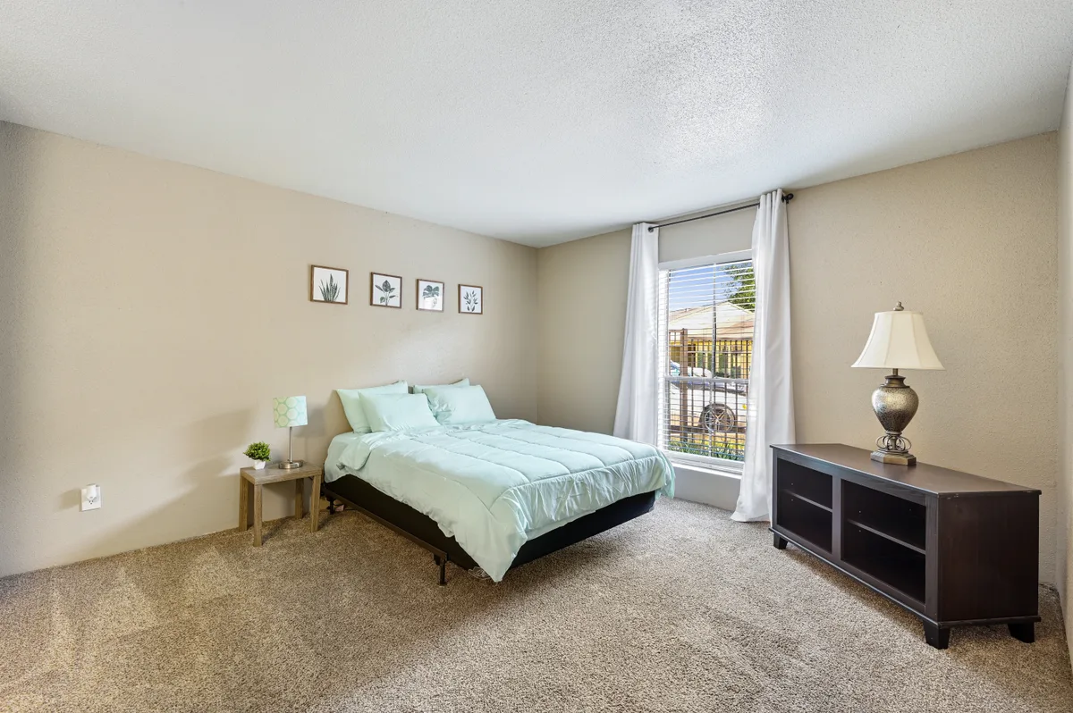 Carpeted bedroom with a queen bed, nightstand, and window with natural light