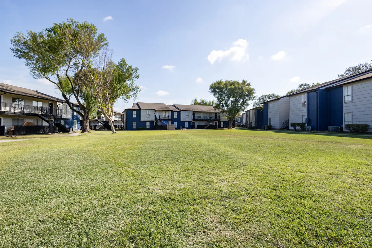 Expansive shaded green lawn stretching between two-story apartment buildings