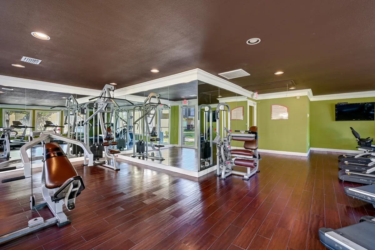 Fitness center with strength machines, a mirrored wall, and warm wood-look flooring