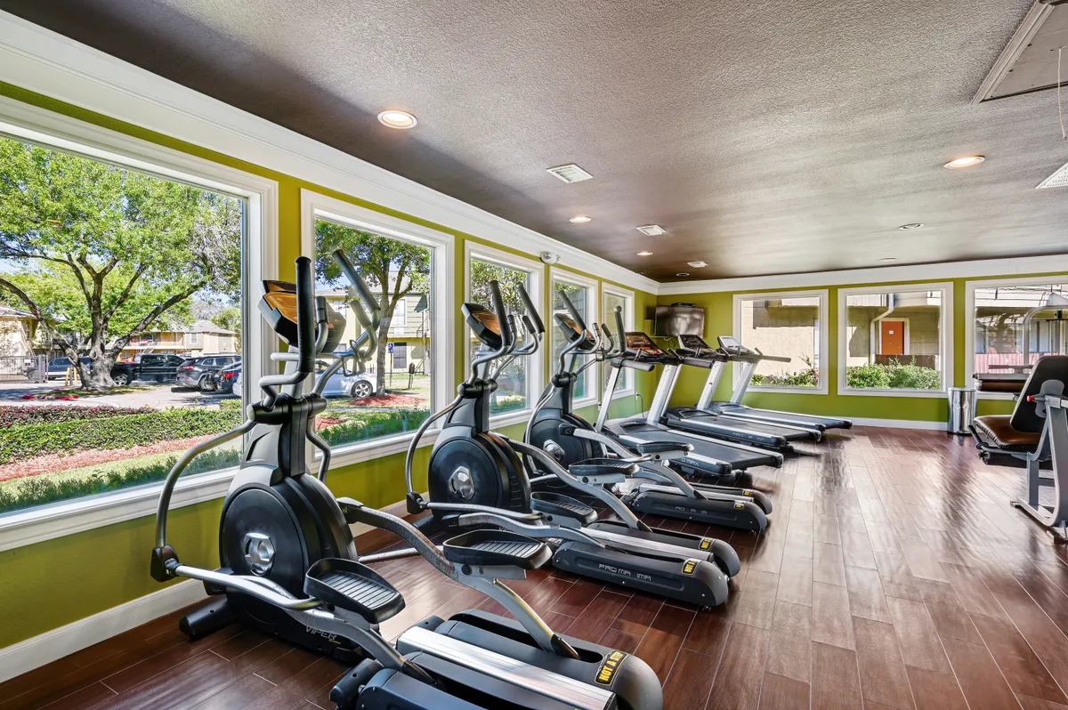 Cardio room lined with treadmills and ellipticals beside bright picture windows