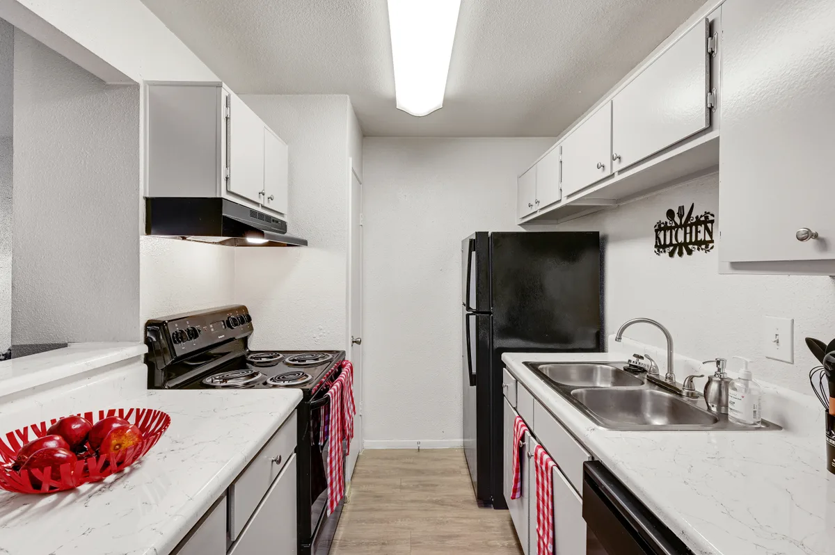 Galley kitchen with white cabinetry, black appliances, and faux-marble countertops