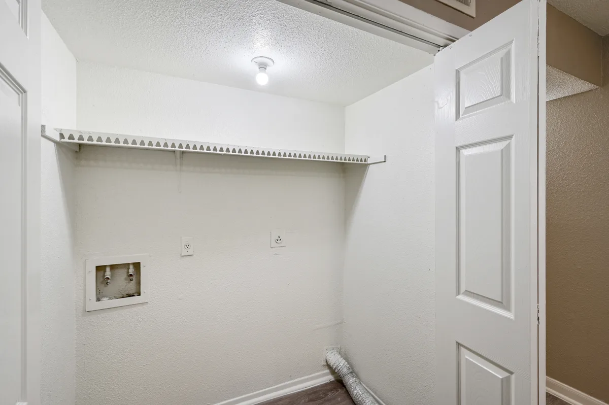 In-unit laundry closet with washer and dryer connections and a storage shelf