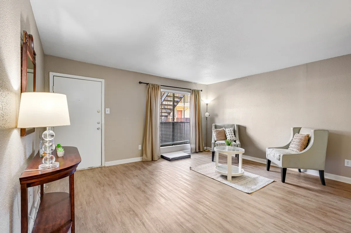 Bright living room with wood-look flooring, accent chairs, and a curtained window