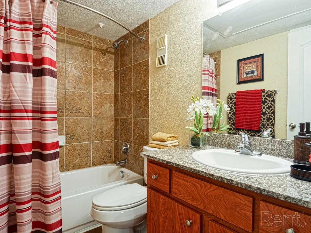 Bathroom with a tiled tub surround, granite-look vanity, and wood cabinetry