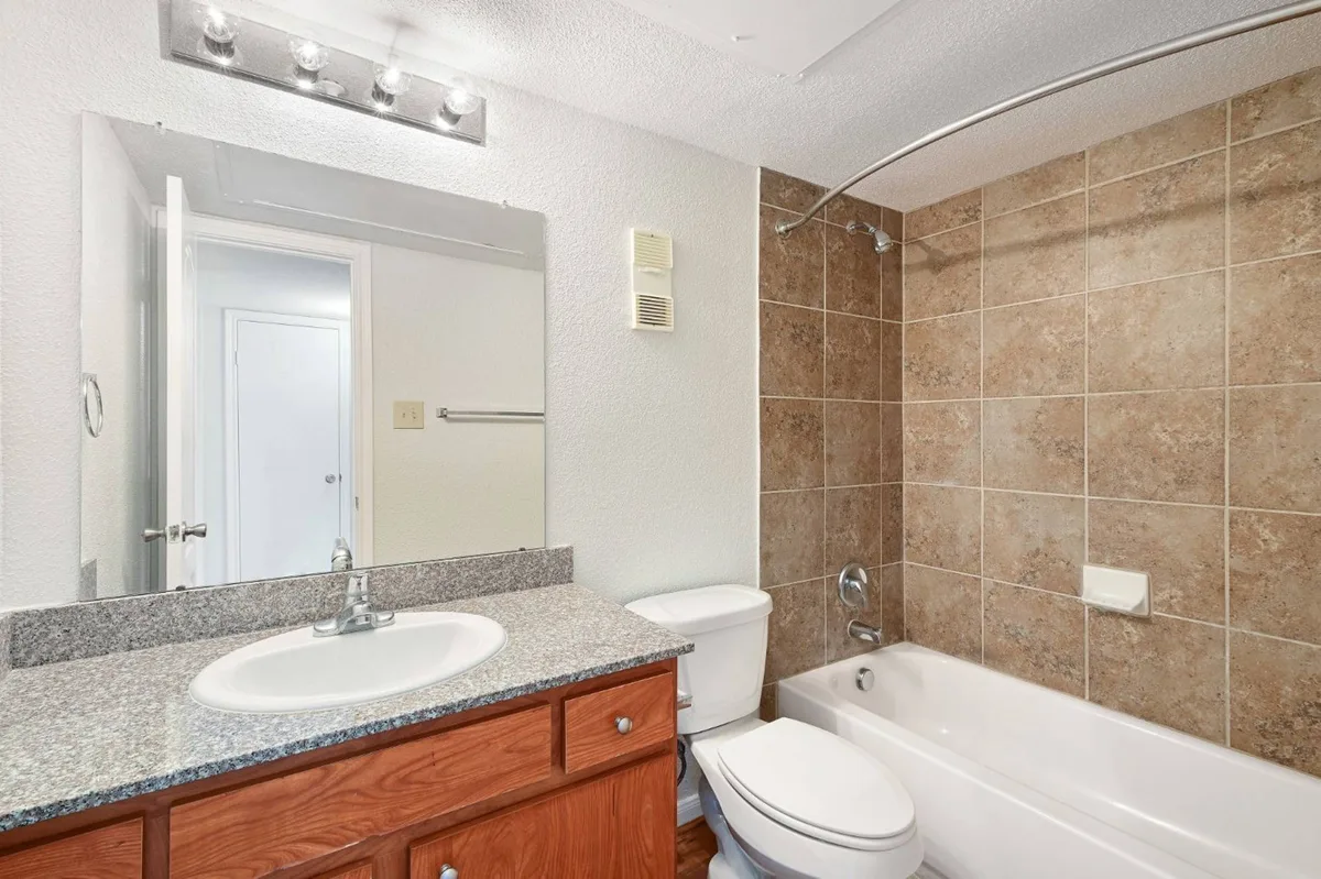 Clean bathroom with a tiled tub surround and granite-topped vanity