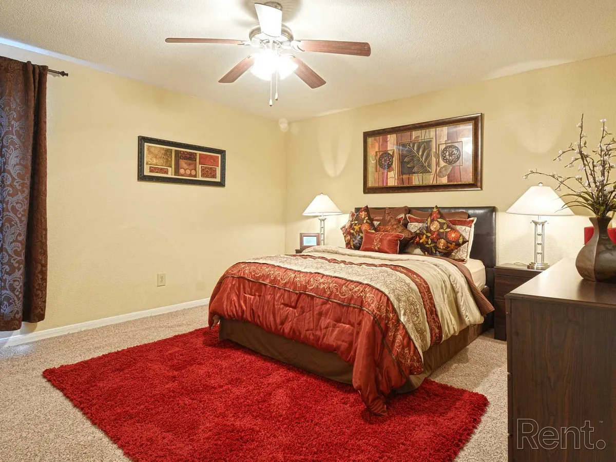 Carpeted bedroom staged with a queen bed and lit ceiling fan