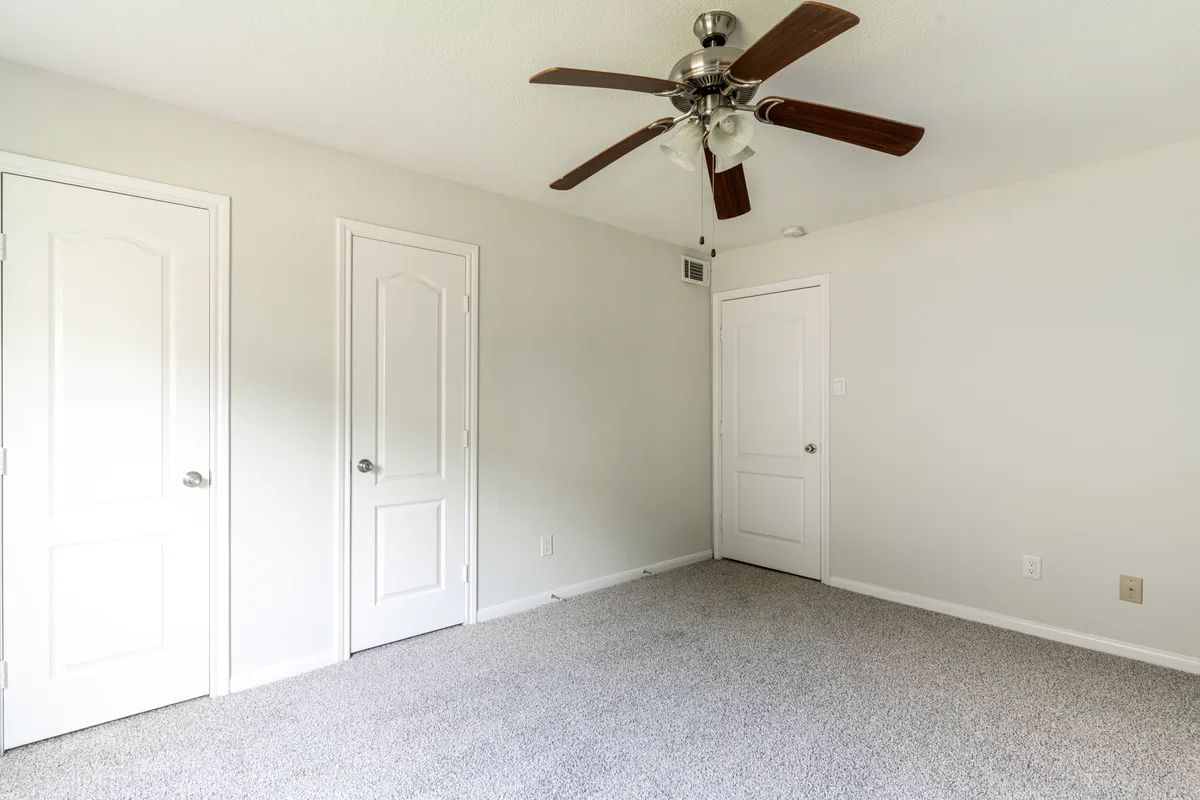 Carpeted bedroom with ceiling fan and two paneled closet doors