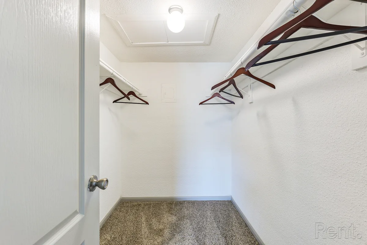Carpeted walk-in closet with wraparound hanging rods and attic access