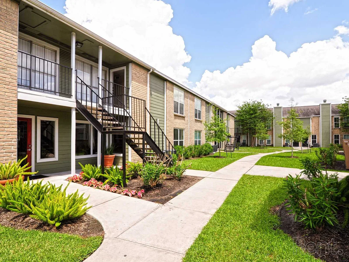 Ground-floor breezeway framed by manicured shrubs and a curving sidewalk