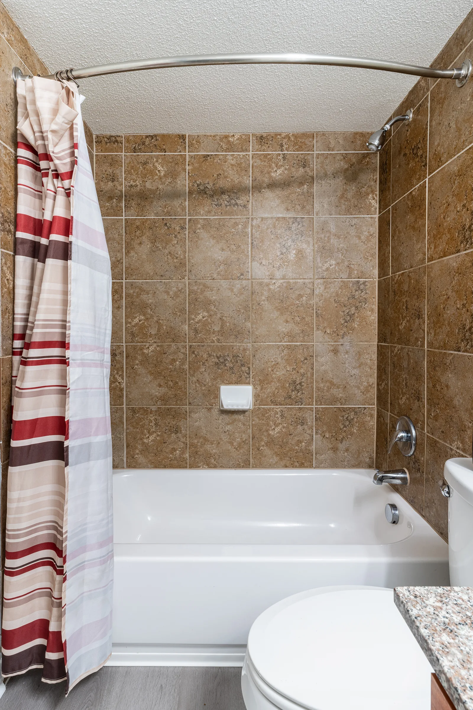 Bathroom with a tiled tub surround, granite vanity, and striped shower curtain