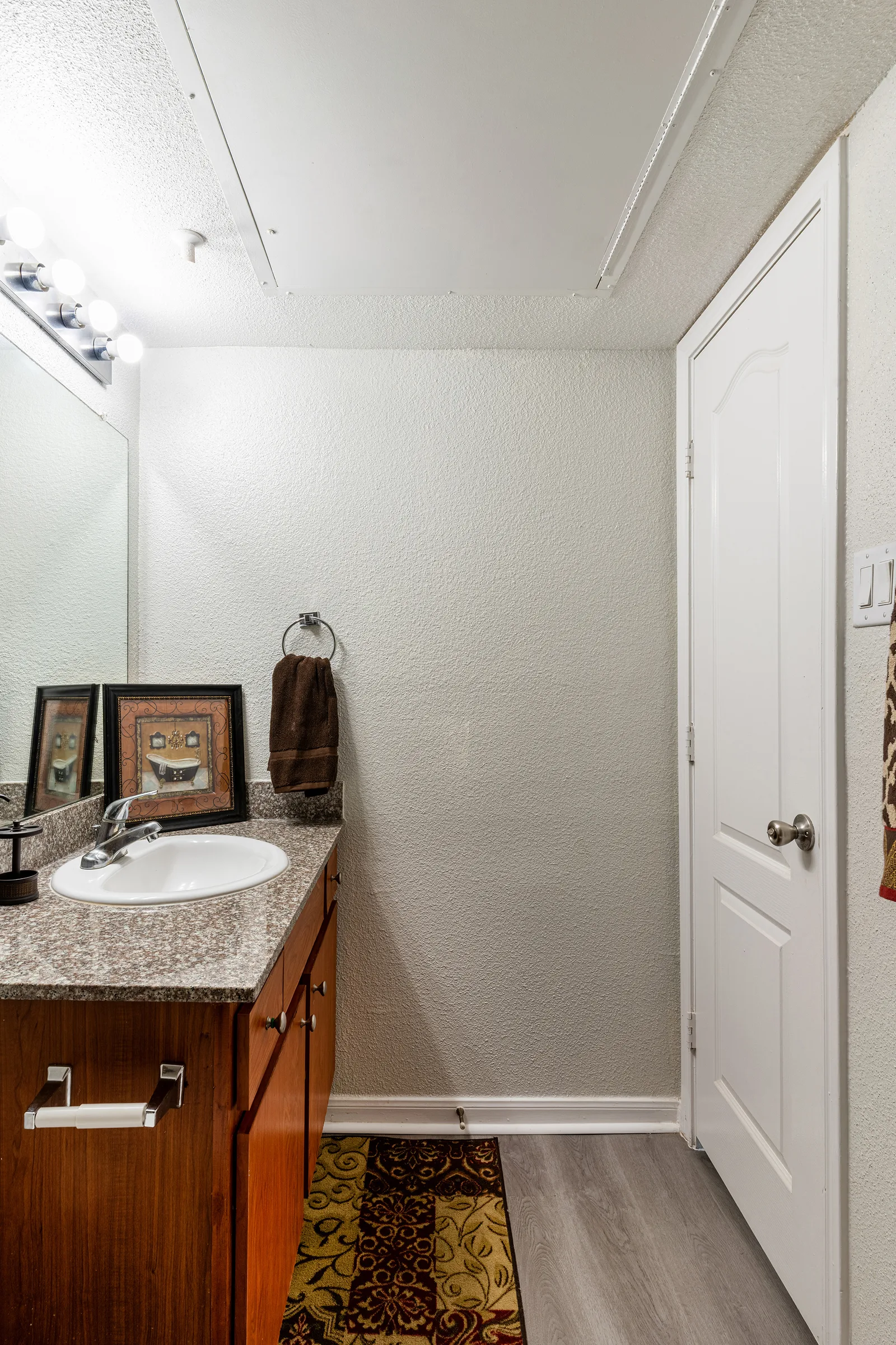 Bathroom with a granite vanity, framed mirror, and wood-look flooring