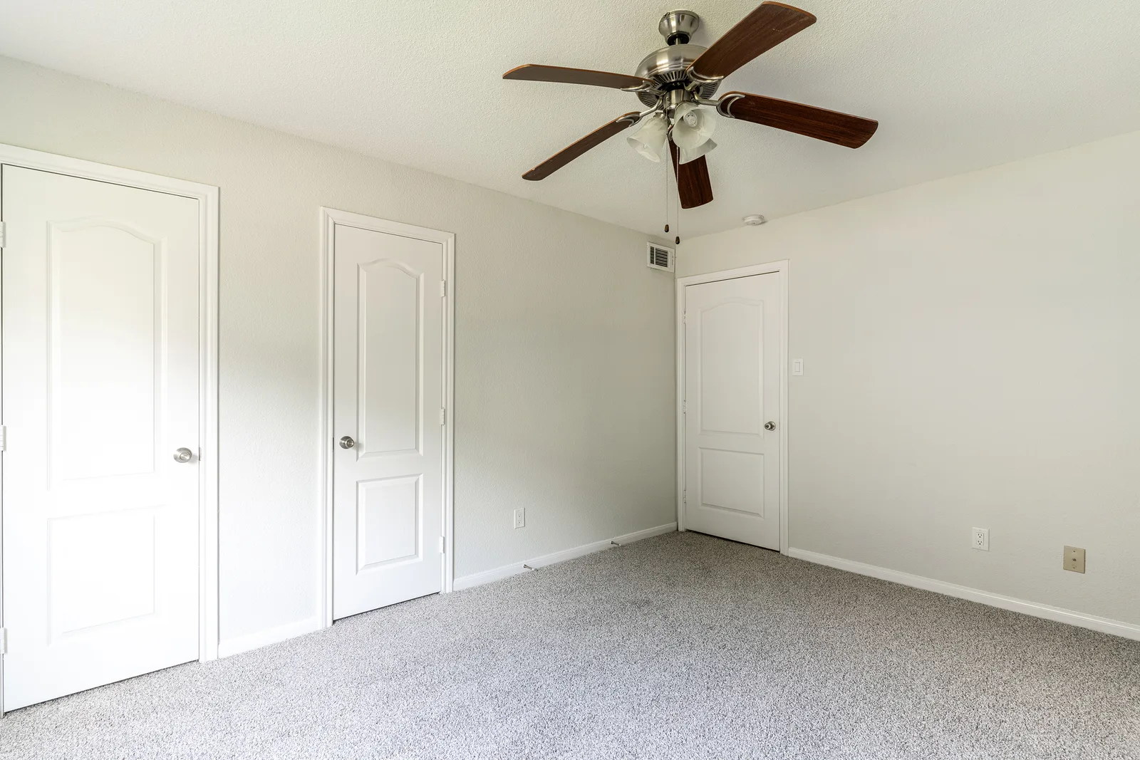Carpeted bedroom with a ceiling fan and two paneled closet doors