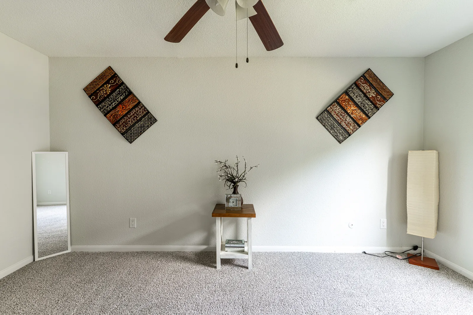 Bright carpeted bedroom with a ceiling fan and a full-length mirror
