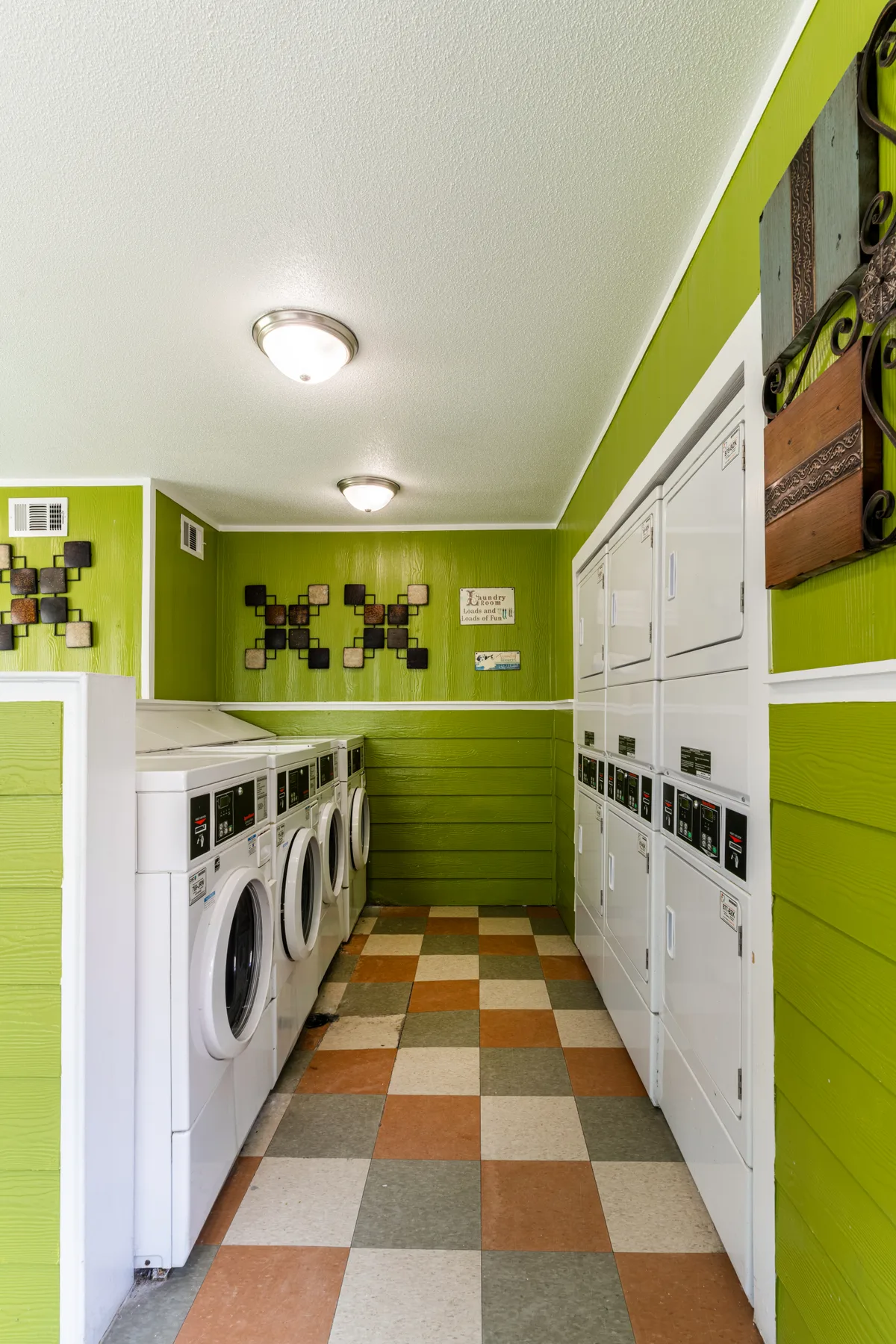 Green-walled laundry room lined with coin-operated washers and stacked dryers
